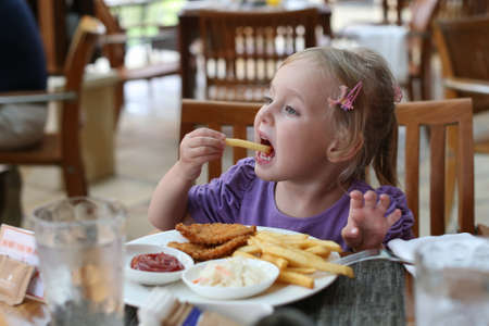 Girl eating French fries. Girl shoves in your mouth fries. The girl at the table dine in fast food. Cafe restaurant outdoors.の写真素材