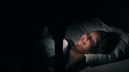 Girl watching movie TV laughing having fun in bed. Attractive blonde Caucasian teen girl in bed at home and watching on phone. Smiling, laughing female. Beautyful white girl lying on bed and use phoneの写真素材