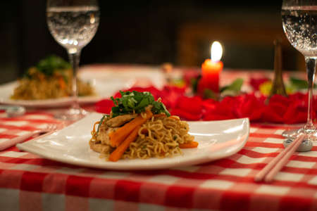 Asian pasta dish in romantic dinner with petals and candleの写真素材