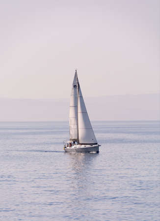 RHODES, GREECE - JUNE 25, 2019: Sailing yacht with white sails on a wavy sea bay