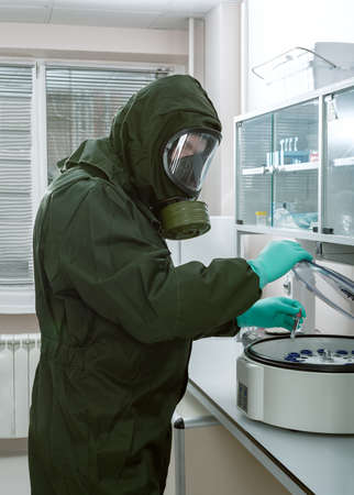 Man in a biohazard protective suit puts test tube with blood in a centrifuge