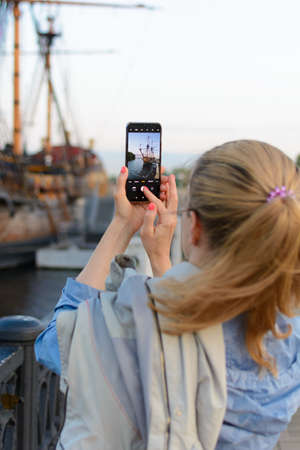 Girl photographing sailing ship on smartphone cameraの写真素材