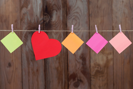 Colored pieces of paper and heart made of paper hanging on a rope on a wooden background with copy spaceの写真素材