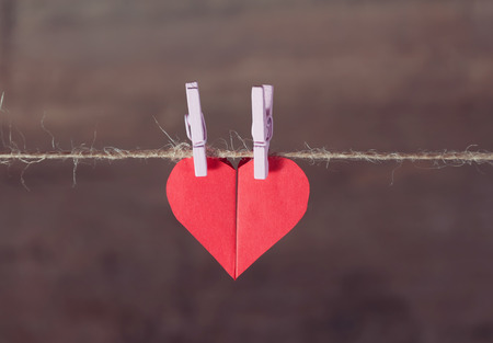 Two paper hearts joined together hanging on a rope on a wooden backgroundの写真素材