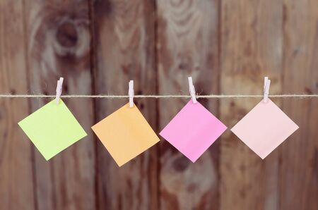 Four colored pieces of paper hanging on a rope on a wooden background with copy spaceの写真素材