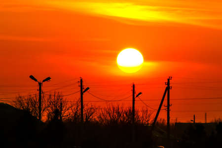 power lines and trees silhouette against an orange sunsetの写真素材