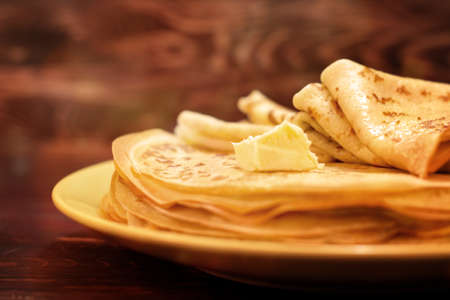 A stack of freshly prepared thin pancakes with melting oil on a wooden tableの写真素材