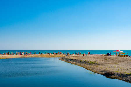 People on the beach in the summer. The river flows into the sea.の写真素材