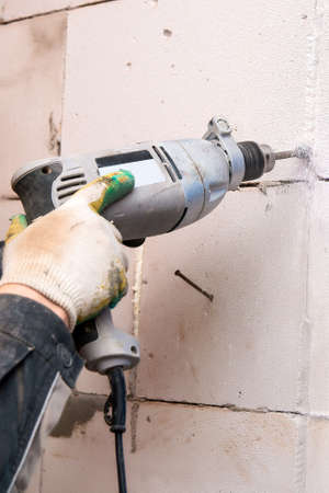 Hands of the Builder drilling the wall at the construction siteの写真素材