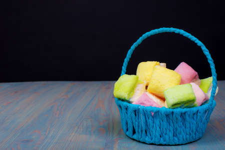 multicolored marshmallow in a blue basket on the table, black backgroundの写真素材