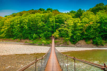 Iron suspension bridge. A suspension bridge leads over a mountain riverの写真素材
