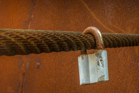 The old lock hangs on a thick rusty iron cableの写真素材