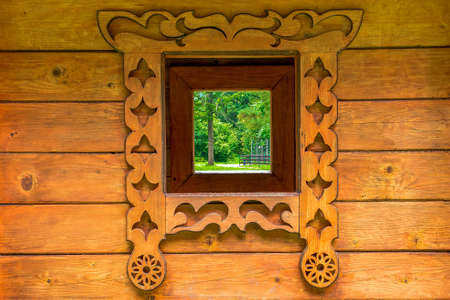 Carved wooden window. Window in a wooden house overlooking the green forestの写真素材