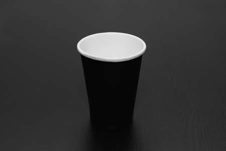 A black coffee paper Cup stands on a black table. Black and white photo