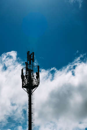 The silhouette of a fifth-generation cellular tower against a background of blue sky and white clouds. Tower with 5g antennasの写真素材