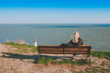 A man sits on a bench with his back and looks at the sea in the distance. A man looks at the seaの写真素材