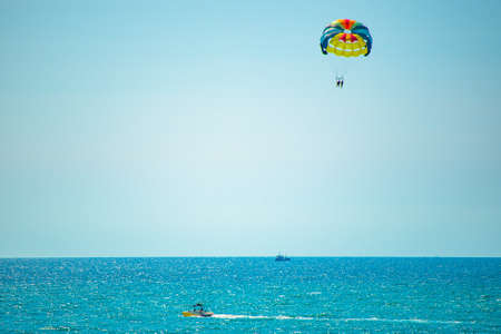 A parachute on a rope flies in the blue sky behind the boat. Beach Parachuteの写真素材