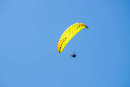 A yellow paraglider flies in the blue skyの写真素材