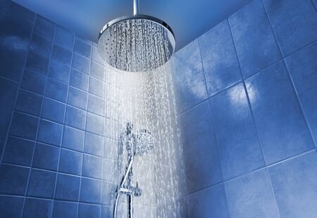 Low angle of running water from shower head in a cool coloured shower in bathroom
