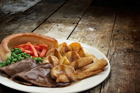Traditional Sunday roast dinner with roast beef, yorkshire pudding and vegetables served in a plate over wooden tableの写真素材