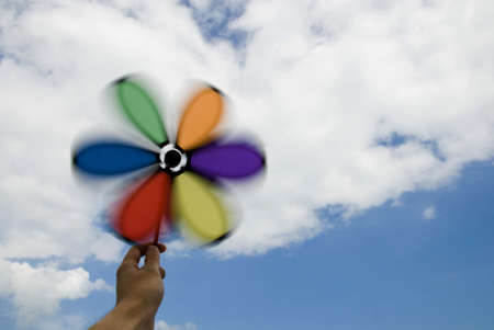 Hand holding spinning wind wheel with cloudy sky の写真素材