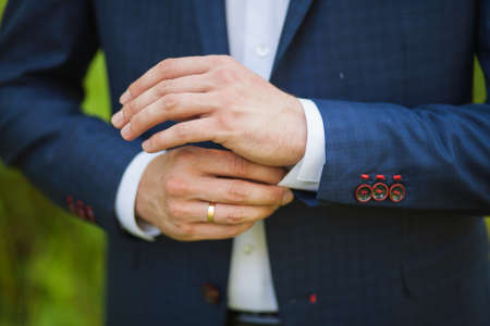 close-up of elegance male hands. man dressed in blue suit and white shirt standing over green nature background. groom in wedding dayの写真素材