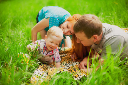 Happy family having fun outdoors. Family picnicking together. Picnic blanket in green grass. Laughing carefree people playing with sonの写真素材