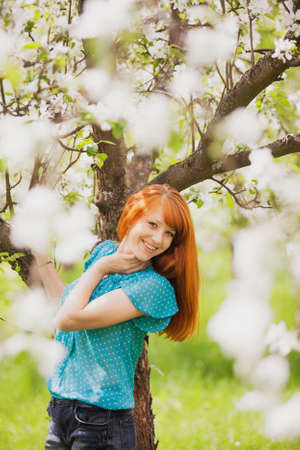 Happy Woman with Gorgeous Red Hair Enjoying Nature. Beauty Young Girl Outdoor in Spring Garden. Freedom concept. Apple-trees in Blossomの写真素材