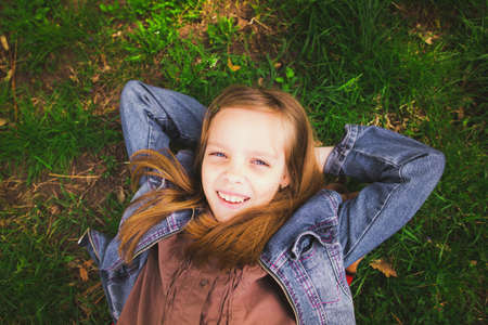 Portrait of young girl laying on grass outdoors. Beautiful smiling child face. Girl looking at camera. Close up. Horizontal color photo.の写真素材