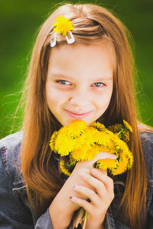Close up portrait of smiling young girl holding bouquet of flowers in hands. Girl with yellow dandelions. Smiling face of teenager with long hear. Vertical color photo.の写真素材