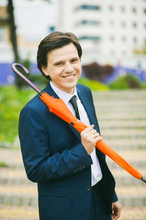 Man with umbrella in hands. Portrait of man in suit. Positive man standing outdoors at city...