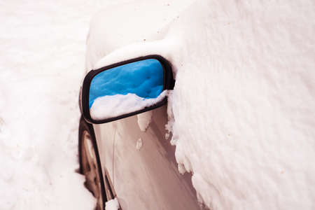 Close up of car covered by snow on snowy winter day. Reflection of fresh snow in automobiles mirror. Horizontal color image.の写真素材