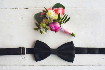 Close up of man accessories. Black bowtie and flower boutonniere on white wood rustic background. Set for formal style of wearing isolated on white wooden background.の写真素材