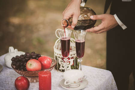 Close up of man hands holding bottle of red wine. Anonymous person pouring drinks in glasses. Man smartly dressed in black suit and white shirt. Preparation for romantic dinner.の写真素材