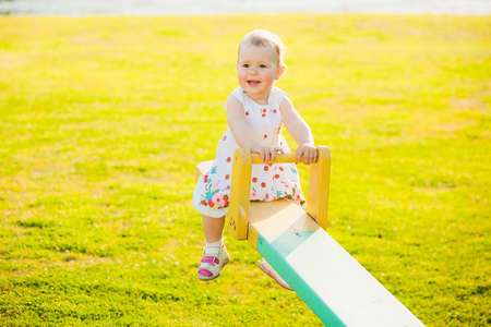 Little girl enjoying riding swing with mum at beautiful nature background. Baby happily playing with parents outside on sunny hot spring or summer dの写真素材