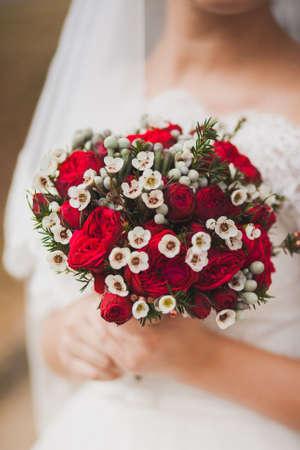 Beautiful wedding bouquet of red roses flowers in hands of anonymous young bride. Image toned and stylized in retro styleの写真素材