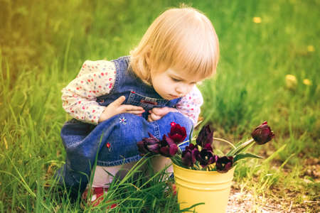 Beautiful small girl wearing denim dress playing alone outside on warm spring day.の写真素材
