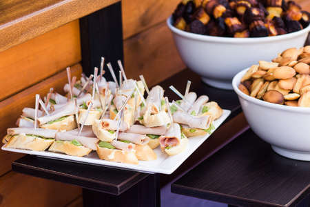 Wood brown tables full of different snacks for party or wedding celebration. White plates with...