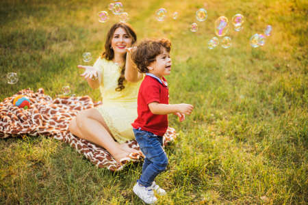 Happy child and woman outdoor playing with soap bubble on meadowの写真素材