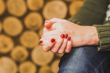 Woman sitting indoors with her hands crossed on knee. Young woman wears green sweater and blue denim...