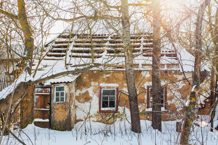Old abandoned empty wooden rural brown house with broken roof and windows covered with fresh white snow. Village in Ukraine. Horizontal color image.の写真素材