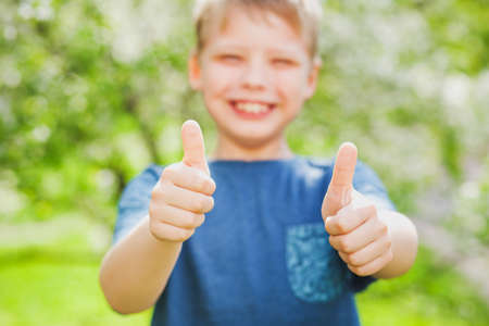 Handsome cheerful 9 years old boy giving two hands with thumbs up into camera as symbol of success....