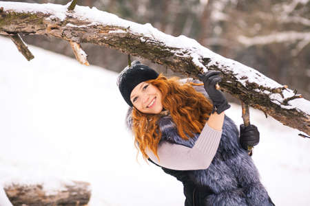Portrait of smiling ginger winter girl looking cheerfully at camera. Closeup of beauty face of young woman in winter fur clothing outside at snowy cold winter day background.の写真素材