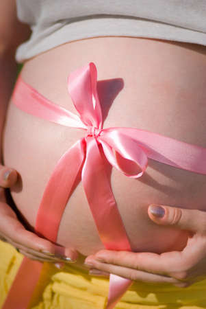 Closeup view of pregnant woman hugging her round big belly with both hands. Vertical color photography.の写真素材