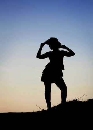 Beautiful happy young cowgirl silhouette isolated at sunset blue sky background. Vertical color photography.の写真素材