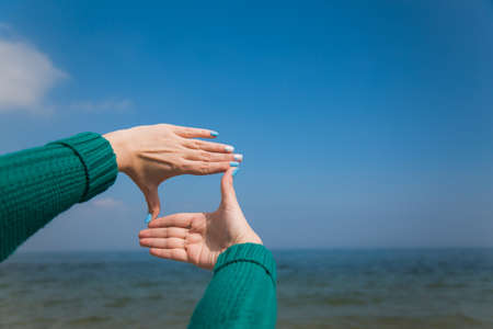 Closeup of female caucasian hands isolated on blue background. Young woman forming frame with her two hands as if looking at something virtual and invisible in sea.の写真素材