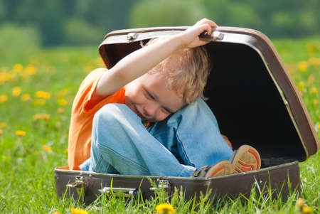 Cute little funny child trying to hide inside of vintage brown suitcase. Boy laughs and smiles happily while playing outdoors on green grass lawn full of yellow dandelion flowers on sunny spring day.
の写真素材