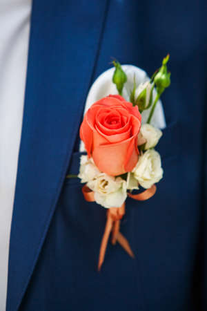 Closeup of beautiful small floral bouquet attached to lapel of blue suit of man. Vertical color photography.の写真素材