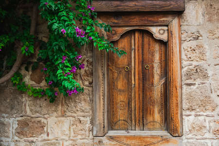 Beautiful wooden closed window in stone wall of old house and green tree with purple flowers growing near it. Horizontal color photography.の写真素材