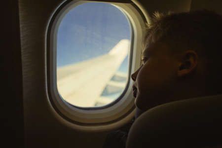 Cute white blond kid looking at window while sitting in his seat during flight. Color photography filtered in vintage style.の写真素材